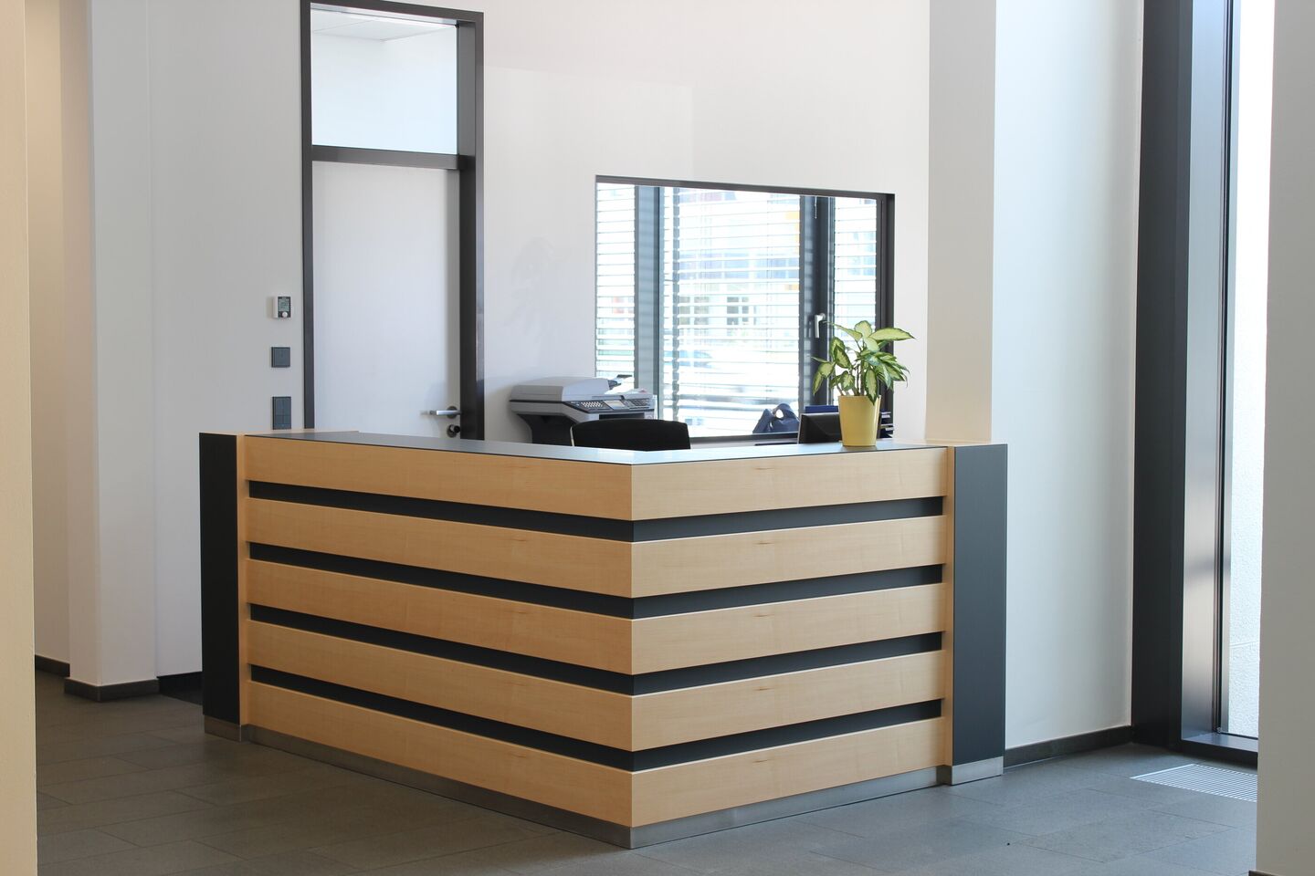 Empfangstheke mit horizontalen Holzlamellen in einem hellen Foyer