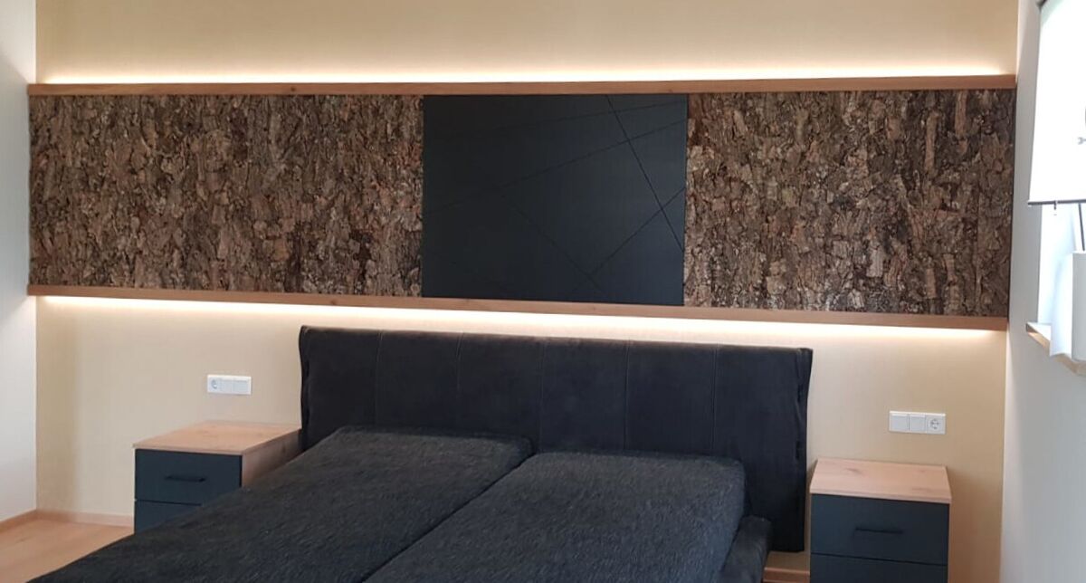 Bett mit breitem Kopfteil aus Holz und indirekter Beleuchtung über die volle Wandbreite