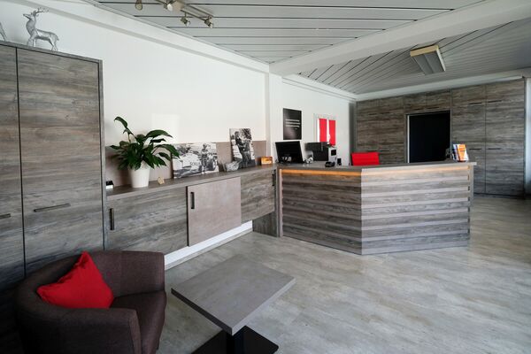 Empfangsbereich mit Theke, Sideboard und Sitzgelegenheit in Holzoptik