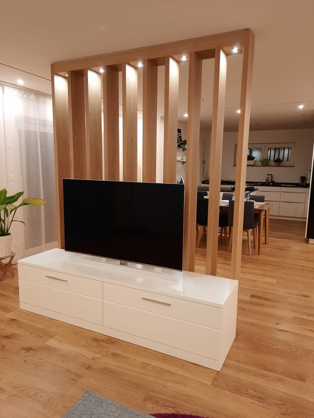 Raumtrenner aus Holzlamellen mit Lowboard und Fernseher zwischen Wohnen und Küche